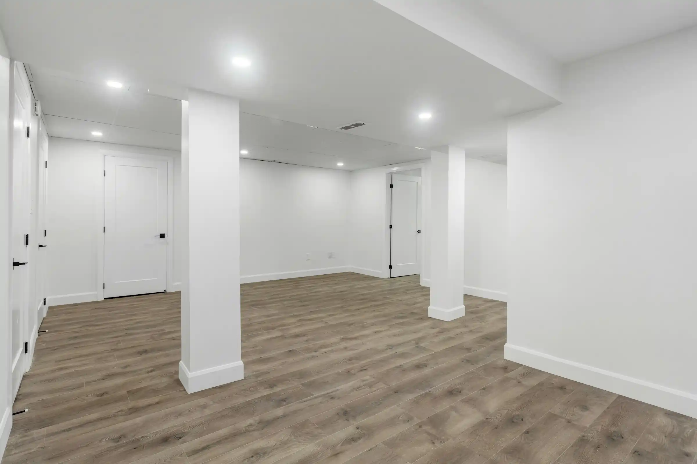 Basement gray wood flooring with white baseboards and doorway trim
